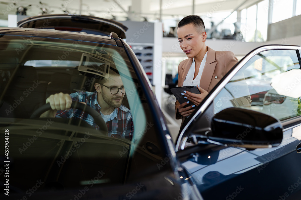 Test drive. Car buyer sitting in auto, choosing new automobile with seller In store.