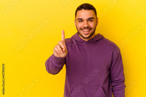 Young caucasian man isolated on yellow background showing number one with finger.