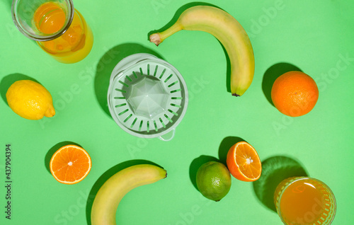 Fototapeta Naklejka Na Ścianę i Meble -  Top view of juice sqeezer, fruits on he green surface.Glass, bottle of fruity drink,banana,oranges,lime,lemon for juice preparation 