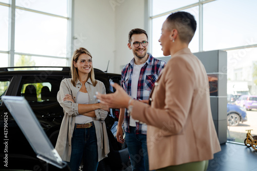 car seller standing in car salon with a customers and discussing about car performances.