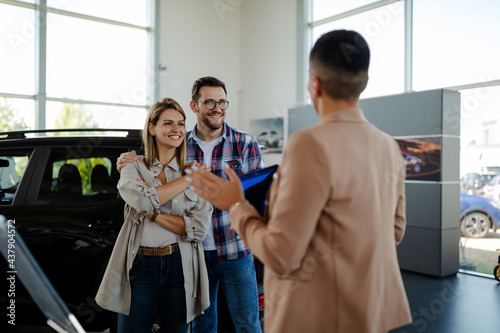 Car seller standing in car salon with a customers and discussing about car performances.