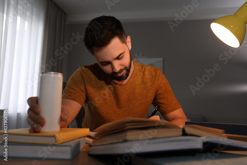 Fotografie Tired young man with energy drink studying at home