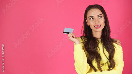 thoughtful young adult woman holding credit card isolated on pink