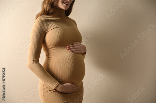 Pregnant woman touching her belly on beige background, closeup. Space for text