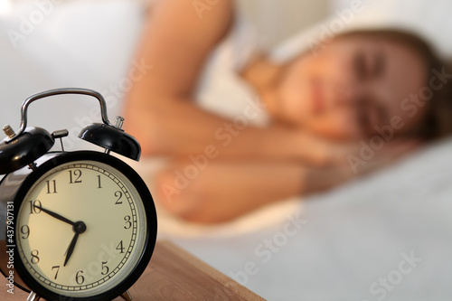 Sleepy young woman stretching hand to ringing alarm willing turn it off. Early wake up, not getting enough sleep, getting work concept.