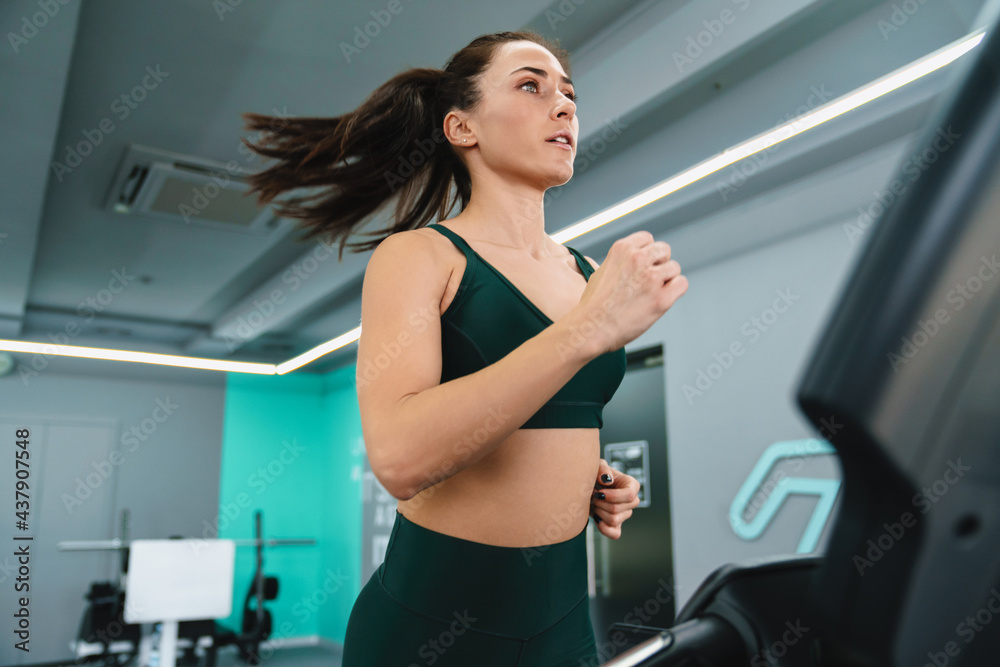 White sportswoman running on treadmill while working out in gym