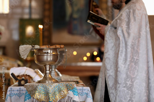 MYKOLAIV, UKRAINE - FEBRUARY 27, 2021: Priest conducting baptism ceremony in Kasperovskaya icon of Mother of God cathedral, focus on vessel with holy water and brush