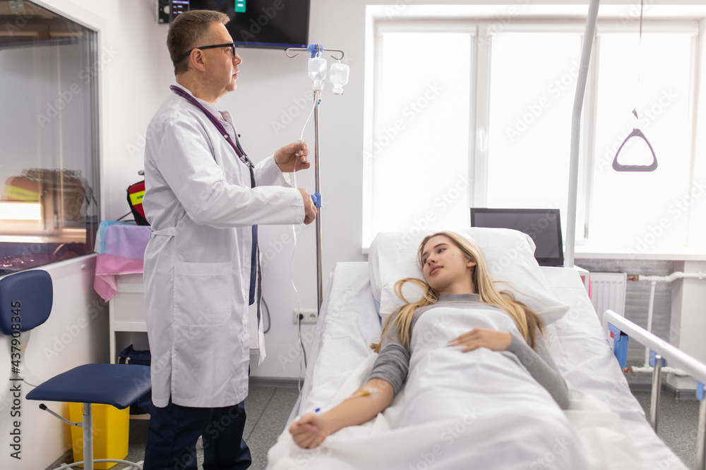 Obraz premium Doctor working, checking Intravenous drip, I.V. tube saline fluid bag for cure patient in hospital room. Handsome professional doctor care his patient by checking I.V. tube saline bag by himself