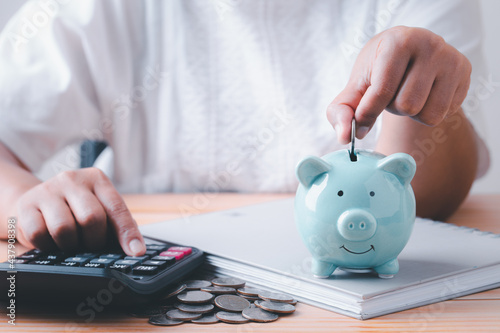 Save money, Woman hand putting coins into blue piggy bank for account save money, Calculate saving money for future rate of return, retirement fund, business investment finance accounting concept.