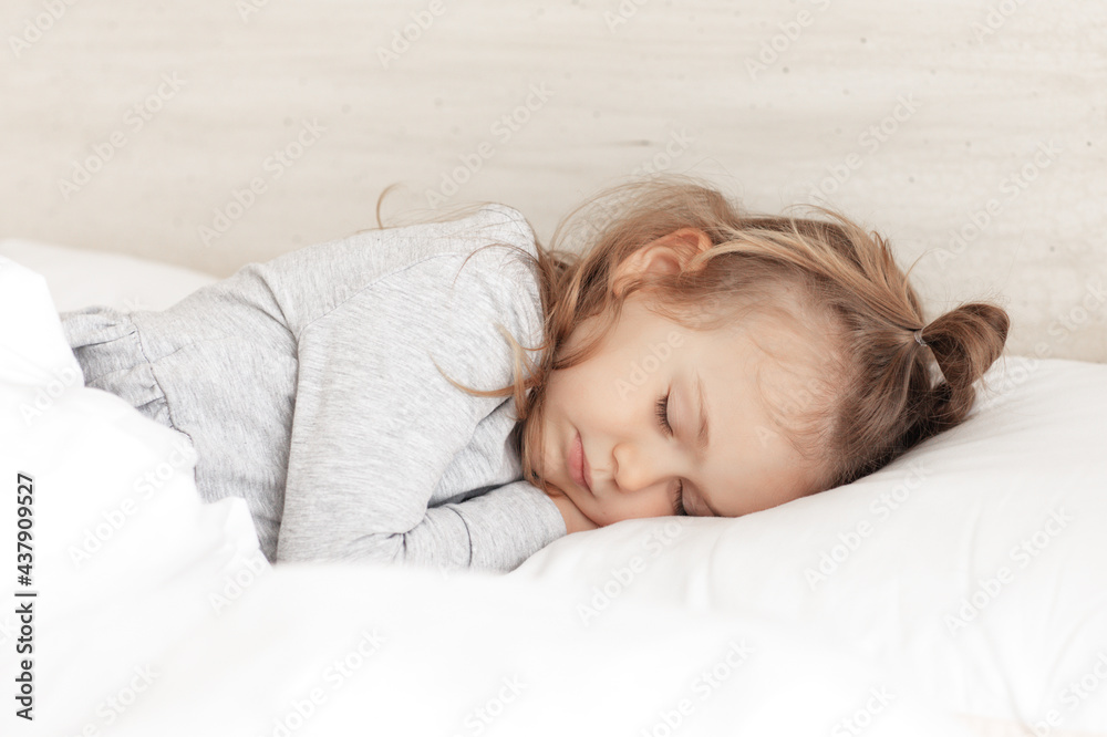 Little adorable child girl in grey pajamas closed eyes lying in bed sleeping on comfortable pillow and under white fluffy cotton blanket, good night sweet dreams Little adorable child girl in grey pajamas closed eyes lying in bed sleeping on comfortable pillow and under white fluffy cotton blanket, good night sweet dreams
