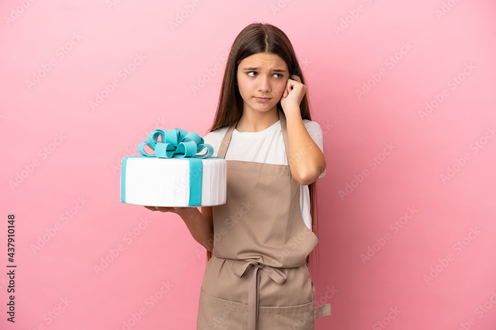 Little girl with a big cake over isolated pink background frustrated and covering ears Little girl with a big cake over isolated pink background frustrated and covering ears