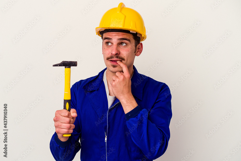 Young caucasian worker man holding a hammer isolated on white background relaxed thinking about something looking at a copy space.