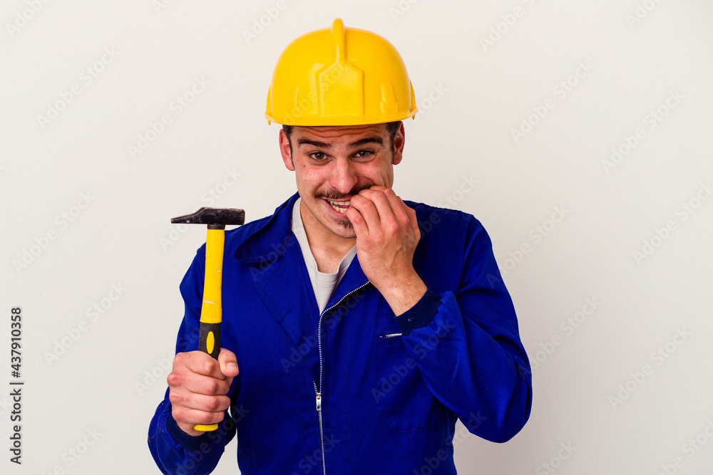 Young caucasian worker man holding a hammer isolated on white background biting fingernails, nervous and very anxious. Young caucasian worker man holding a hammer isolated on white background biting fingernails, nervous and very anxious.