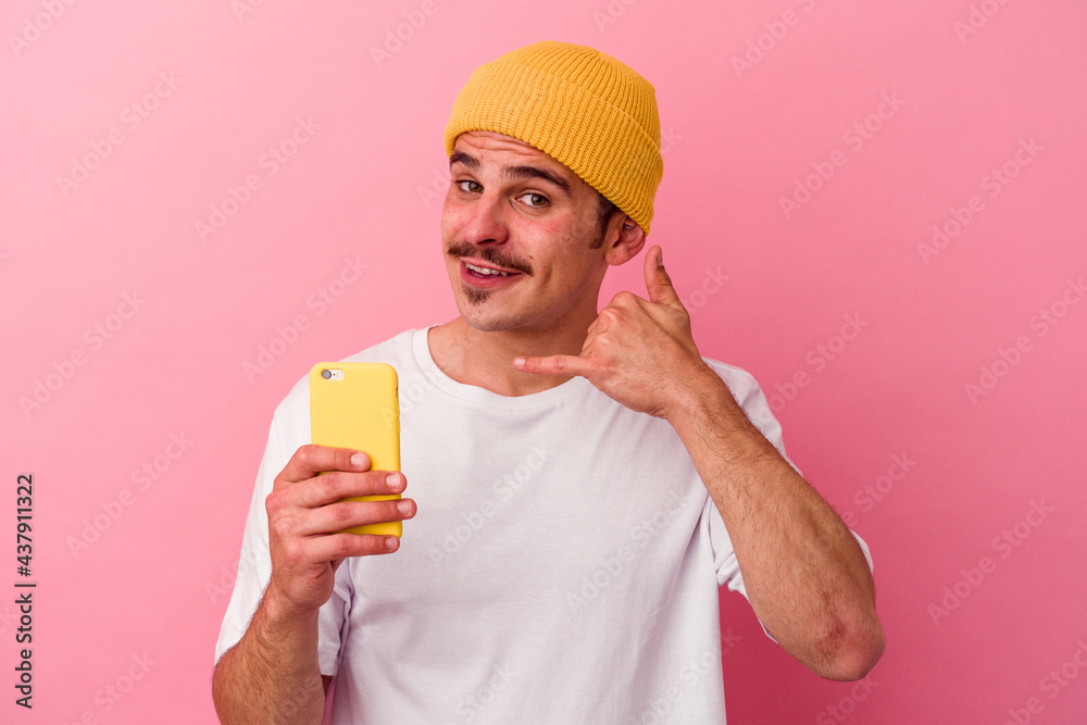 Young caucasian man holding a mobile phone isolated on pink background showing a mobile phone call gesture with fingers. Young caucasian man holding a mobile phone isolated on pink background showing a mobile phone call gesture with fingers.