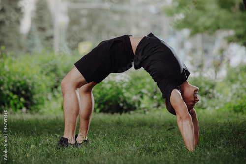 Sporty fit man doing yoga bridge pose in a park