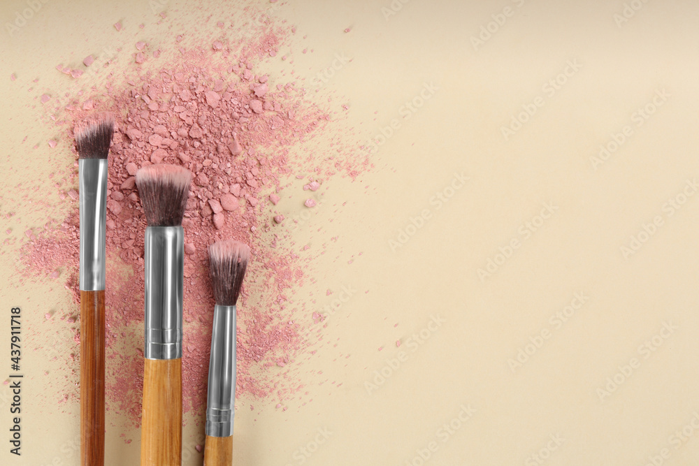 Fototapeta premium Makeup brushes and scattered eye shadow on beige background, flat lay. Space for text