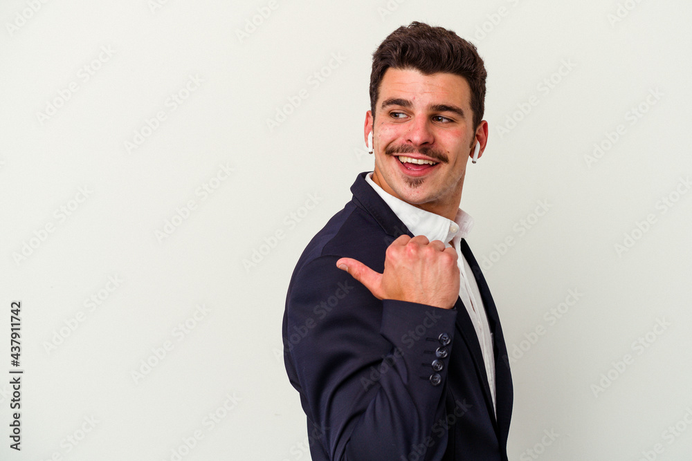 Young business caucasian man wearing wireless headphones isolated on white background points with thumb finger away, laughing and carefree. Young business caucasian man wearing wireless headphones isolated on white background points with thumb finger away, laughing and carefree.