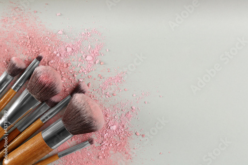 Slika na platnu Makeup brushes and scattered eye shadows on light grey background, flat lay