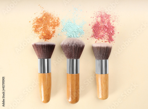 Makeup brushes and scattered eye shadows on beige background, flat lay