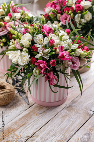 Gift bouquets of flowers to a cardboard box, packing twine and scissors. Pink rose and alstrameria in a round gift box on a wooden background. Vertical shot. Copy space.