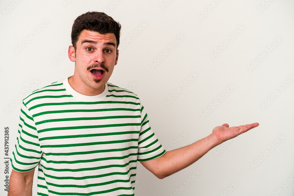 Young caucasian man isolated on white background impressed holding copy space on palm. Young caucasian man isolated on white background impressed holding copy space on palm.