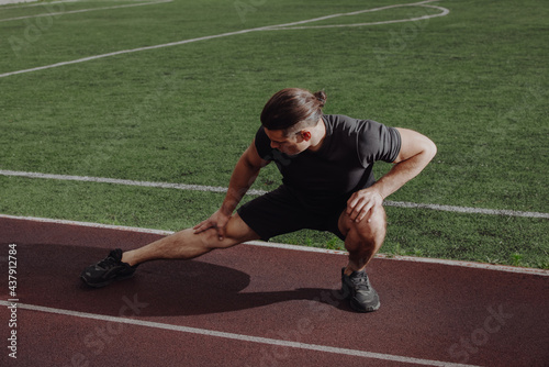 Athlete sporty man stretches leg before running on a stadium