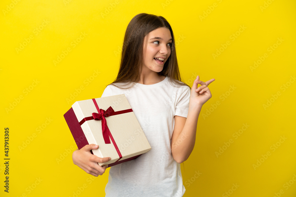 Little girl holding a gift over isolated yellow background intending to realizes the solution while lifting a finger up Little girl holding a gift over isolated yellow background intending to realizes the solution while lifting a finger up
