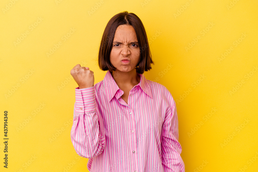 Fototapeta premium Young mixed race woman isolated on yellow background showing fist to camera, aggressive facial expression.
