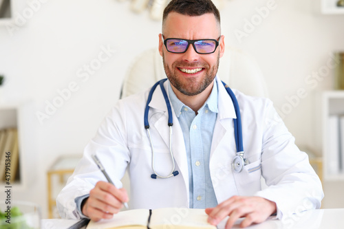 Positive professional male physician therapist in white coat with stethoscope smiling at camera