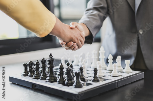 Two business women shake hands after playing a game of chess, playing a game of chess is like planning a business plan and having to solve problems. Business risk management concept.