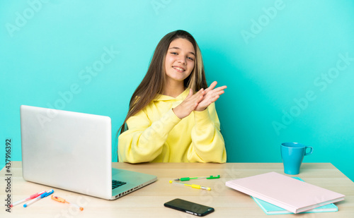 Little girl in a table with a laptop over isolated blue background applauding after presentation in a conference