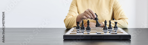 A businesswoman holding a black chess piece walks forward on a chessboard, comparing the chessboard to business administration, planning operations to achieve goals and solve business problems.