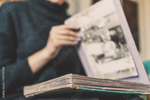 Close-up of a girl in dark clothes sitting on the sofa, holding an album on her lap and looking at old photos