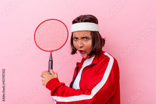 Young mixed race woman playing badminton isolated on pink background © Asier