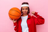 Young mixed race woman playing basketball isolated on pink background showing a dislike gesture, thumbs down. Disagreement concept.