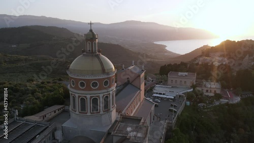 Aerial still shot of Sanctuary of Tindari  baroque dome style architecture, high angle drone view at sunset of mediterranean coastline with sun flare, iconic Sicily vacation destinations in Italy photo