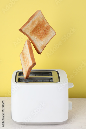 Bread slices popping up from modern toaster on white wooden table