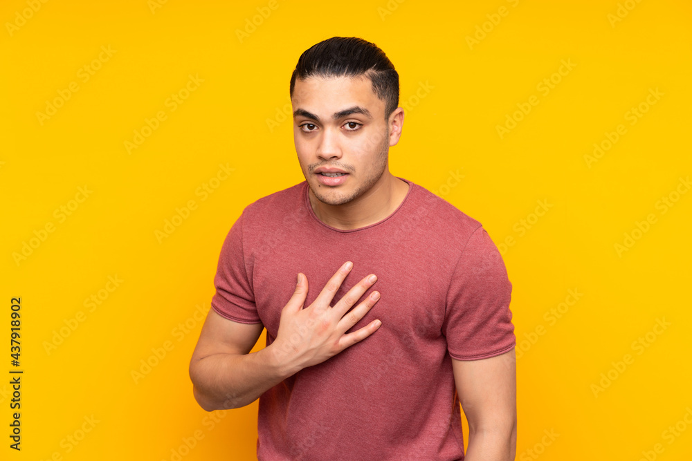 Asian handsome man isolated on yellow background keeps palm together. Person asks for something Asian handsome man isolated on yellow background keeps palm together. Person asks for something