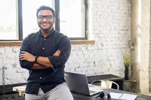 Фотография Ambitious hindu man in smart casual shirt stands with arms crossed in contemporary office space and looks at camera, portrait of purposeful indian businessman, ceo indoor