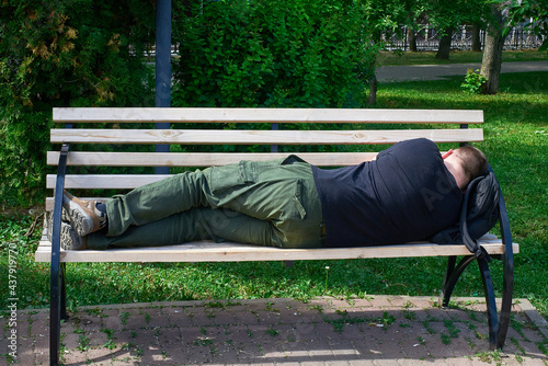 A tired tourist sleeps on a bench in the park, putting a backpack under his head.