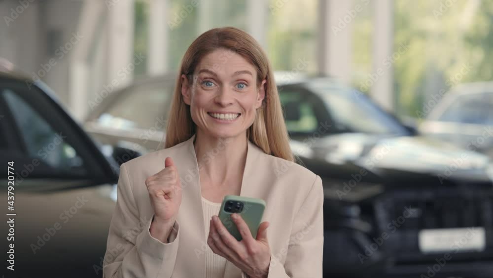 Happy woman using smartphone while buying car at dealership