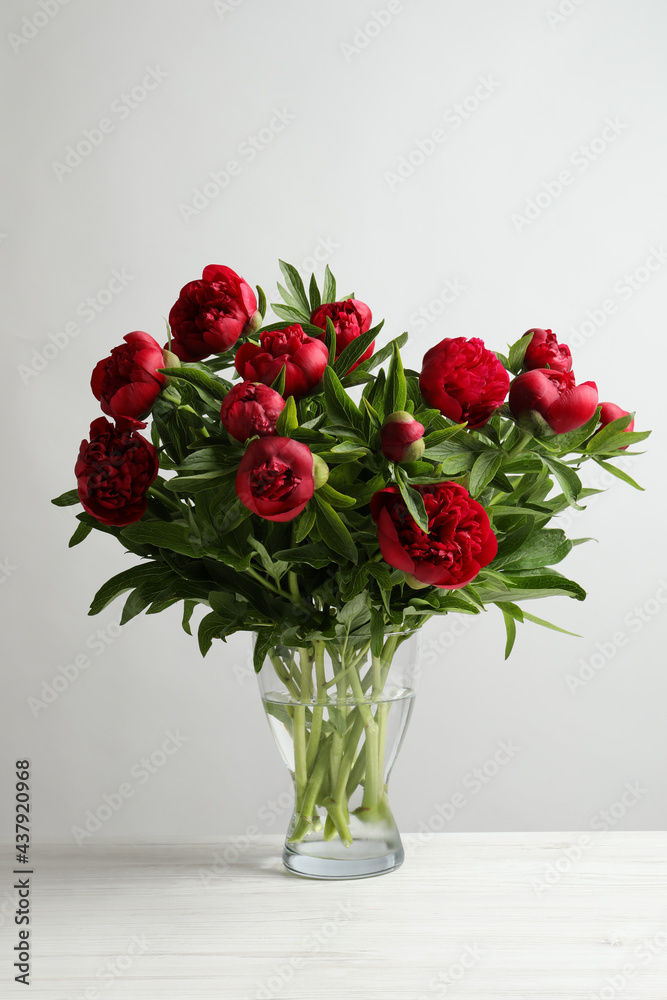 Beautiful bouquet of red peony flowers in glass vase on white table