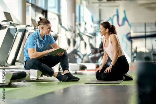 Happy athletic woman talking to her personal trainer during break in a gym.