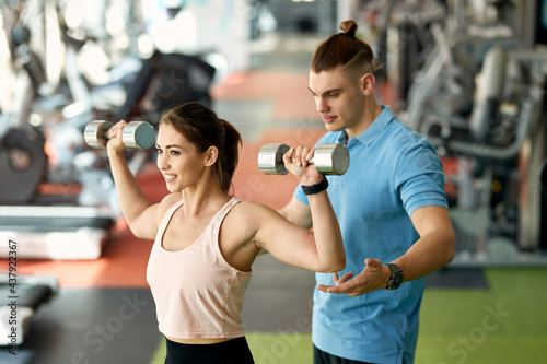Fototapeta Naklejka Na Ścianę i Meble -  Young sportswoman using hand weights while having sports training with fitness instructor in a gym.