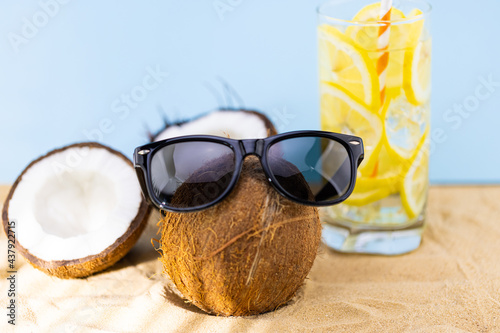 stylish coconut in sunglasses and a glass of lemonade on the sand. Summer vacation concept