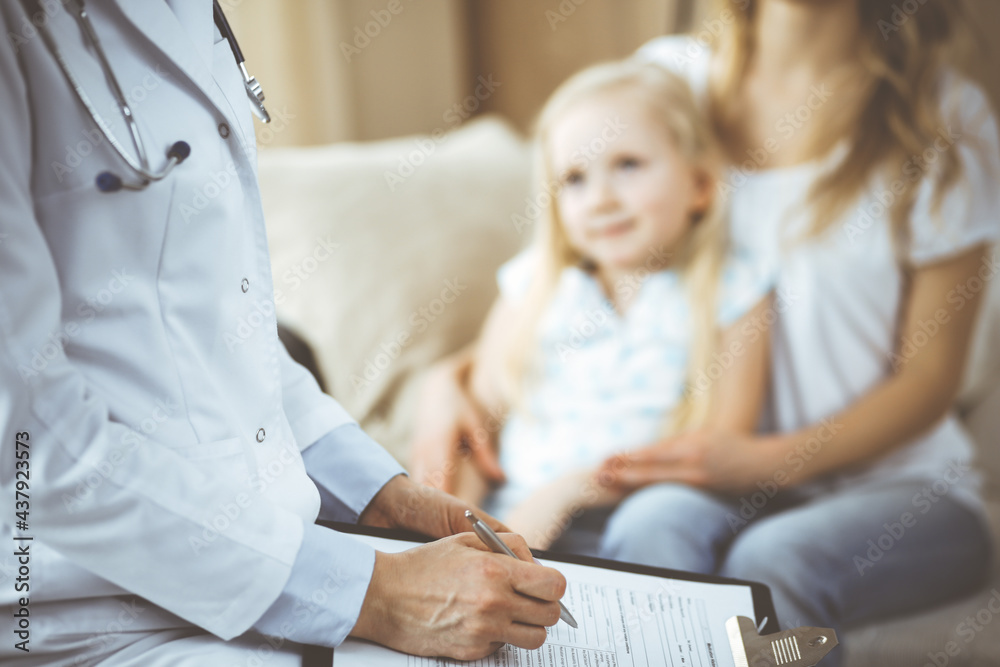Fototapeta premium Doctor and patient. Pediatrician using clipboard while examining little girl with her mother at home. Happy cute caucasian child at medical exam. Medicine concept