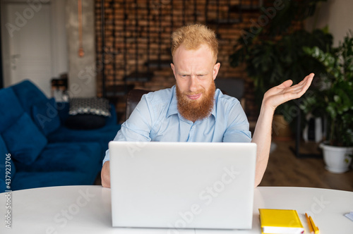 Fototapeta Puzzled and confused redhead bearded male entrepreneur staring at the laptop scr