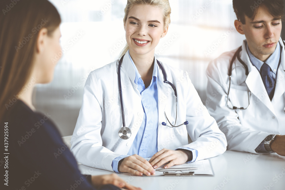 Woman-doctor with male colleague are consulting patient woman while sitting at the desk in modern clinic. Perfect medical service, medicine concept Woman-doctor with male colleague are consulting patient woman while sitting at the desk in modern clinic. Perfect medical service, medicine concept