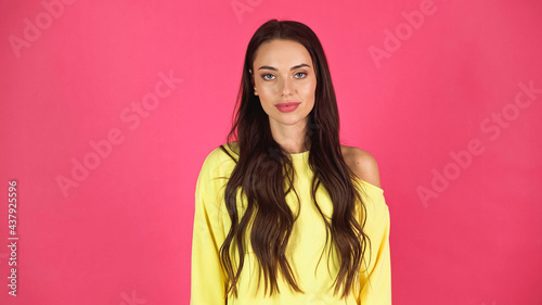 young adult woman in yellow blouse looking at camera isolated on pink