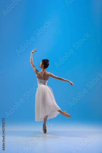Young and incredibly beautiful ballerina is posing and dancing at blue studio full of light.